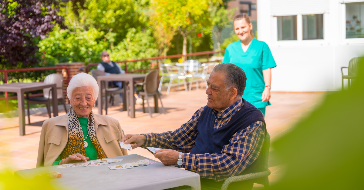 Twee oudere mensen met de verpleegkundige in de tuin van een verpleeghuis of bejaardentehuis die kaartspelen