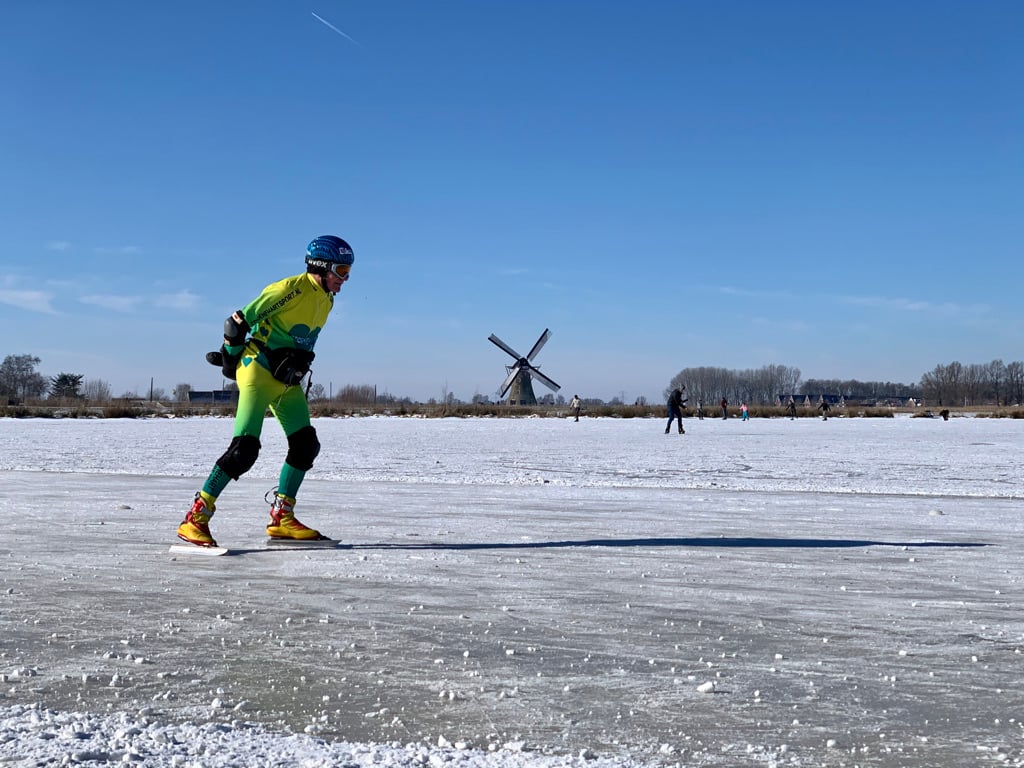 Skaters on a frozen lake with farms and a windmill in the background