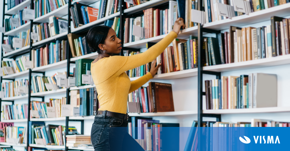 Young  woman in casual outfit taking textbook from bookcase  in library of modern university